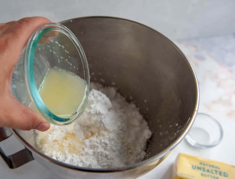 adding pasteurized egg whites to powdered sugar in a metal bowl