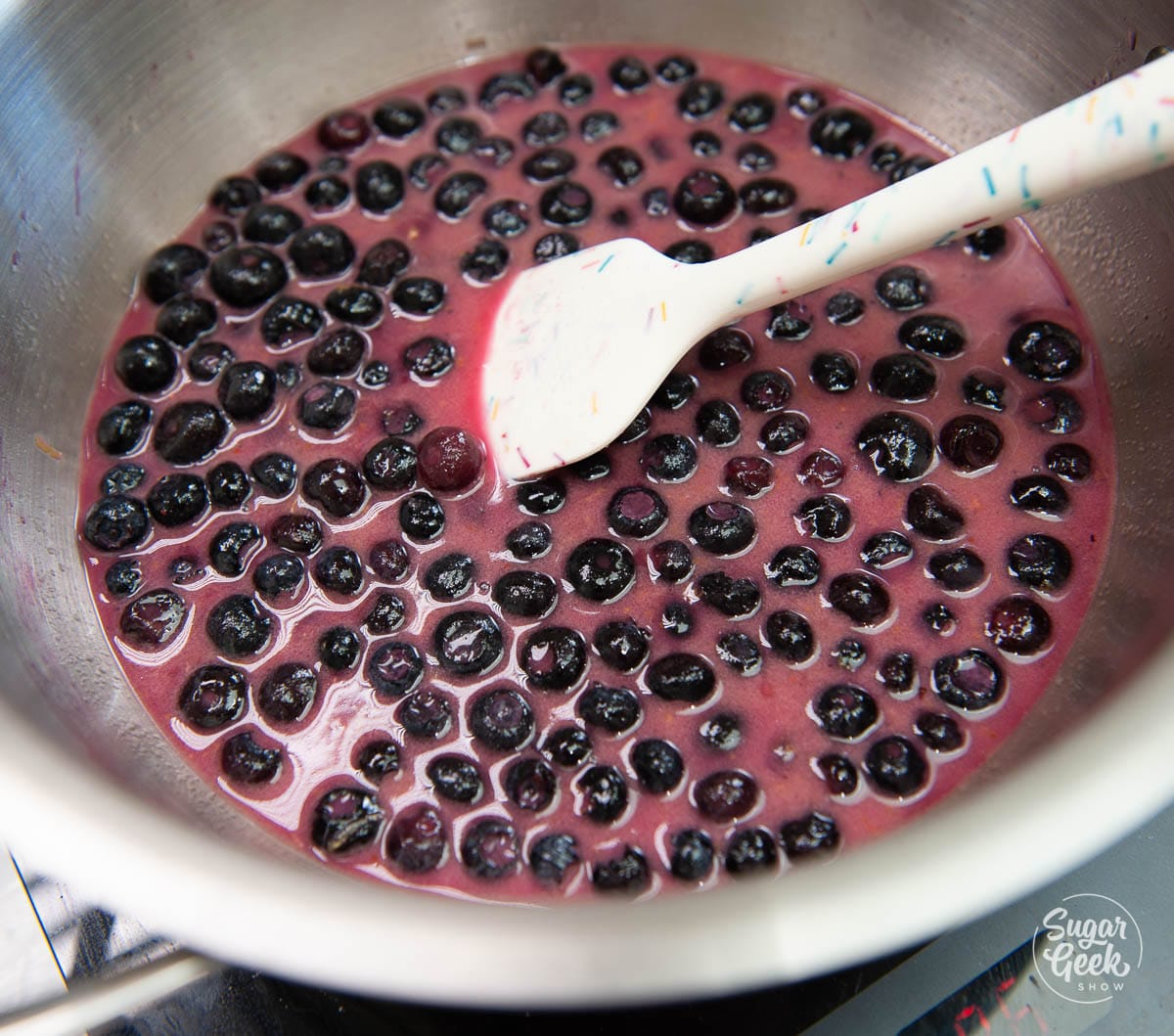 blueberries with cornstarch mixture in a stainless steel pot with a white spoon