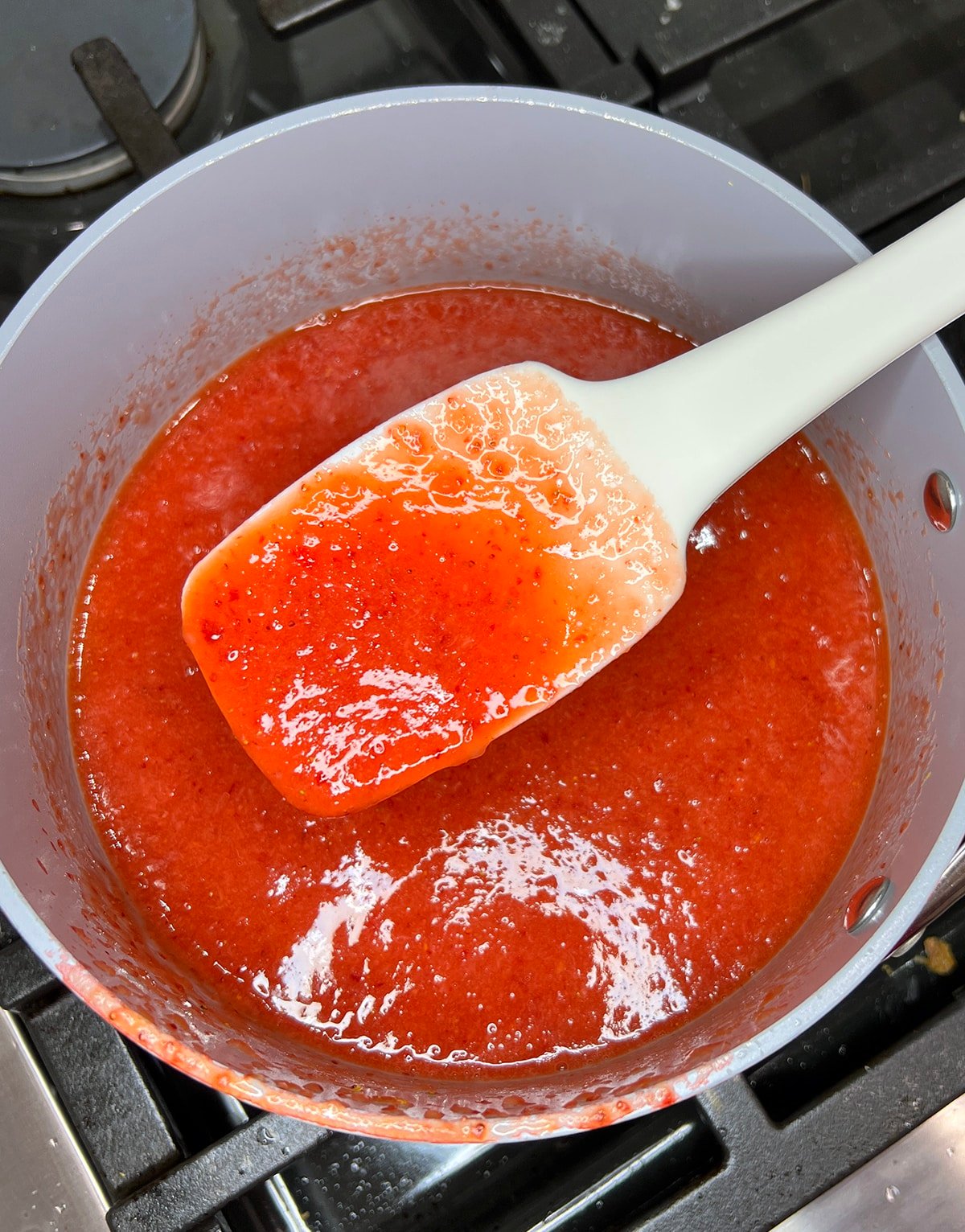 close up of blended strawberries in a saucepan with a rubber spatula