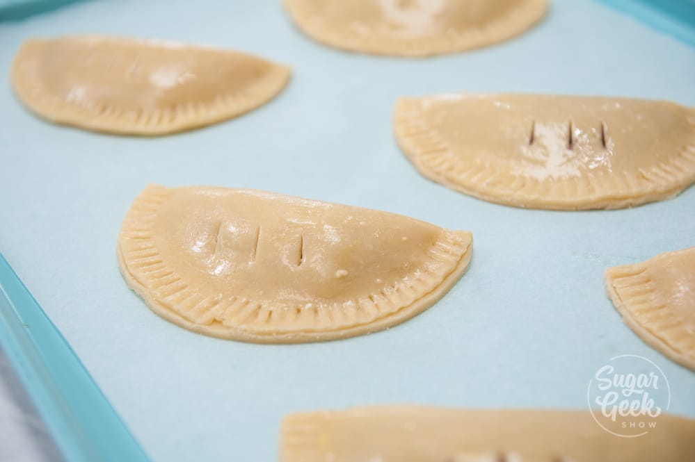close up of hand pies on a blue baking sheet with parchment paper