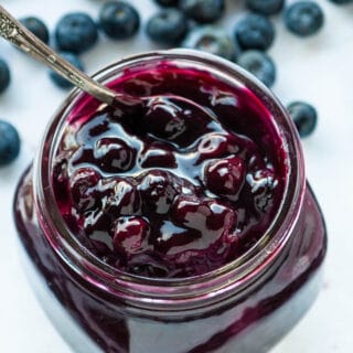 close up of homemade blueberry filling in a clear jar with a spoon