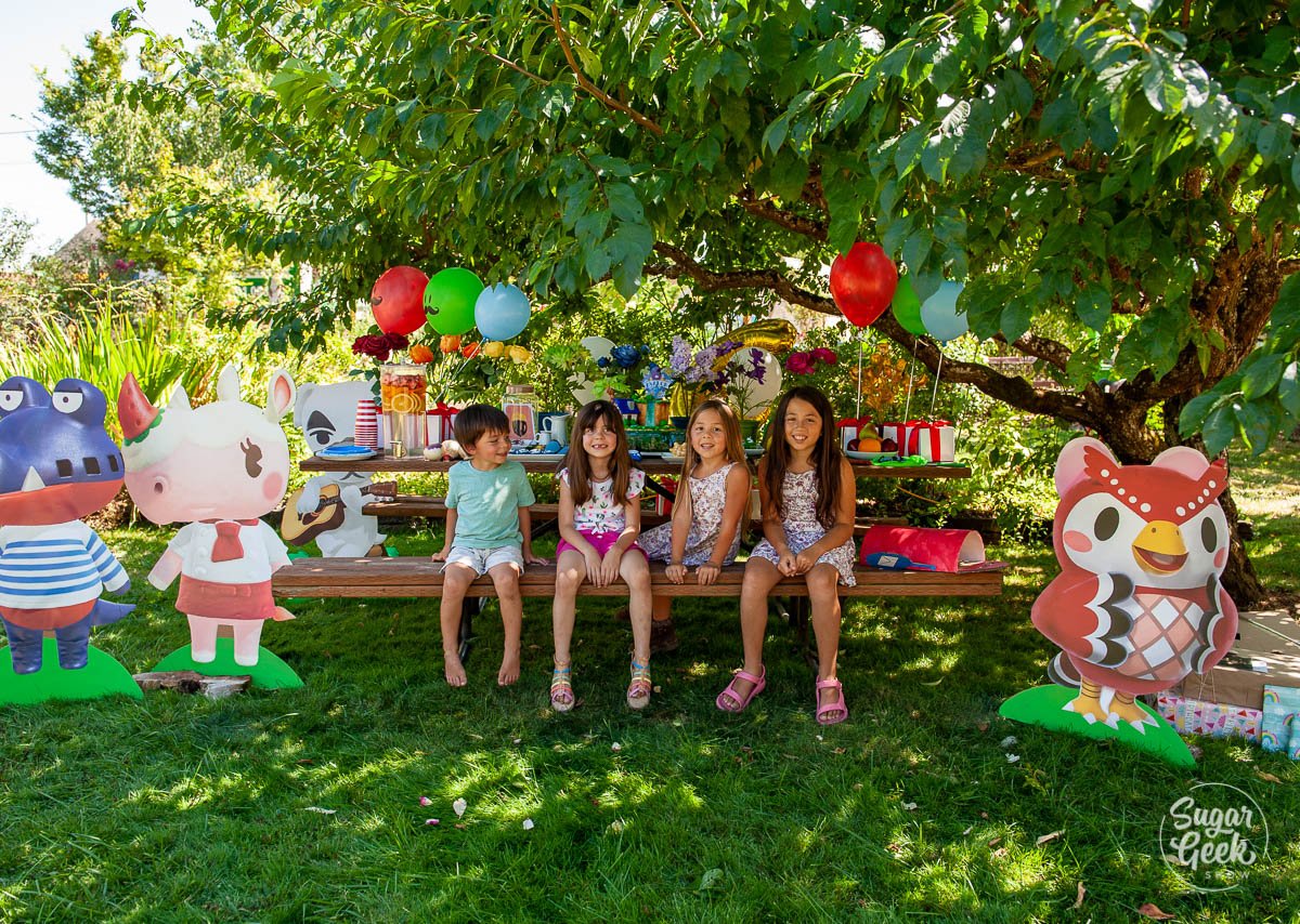 four kids sitting on a picnic bench with birthday decorations under a tree