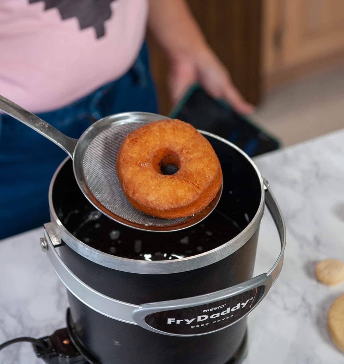 close up of donut on a slotted spoon over a fry daddy