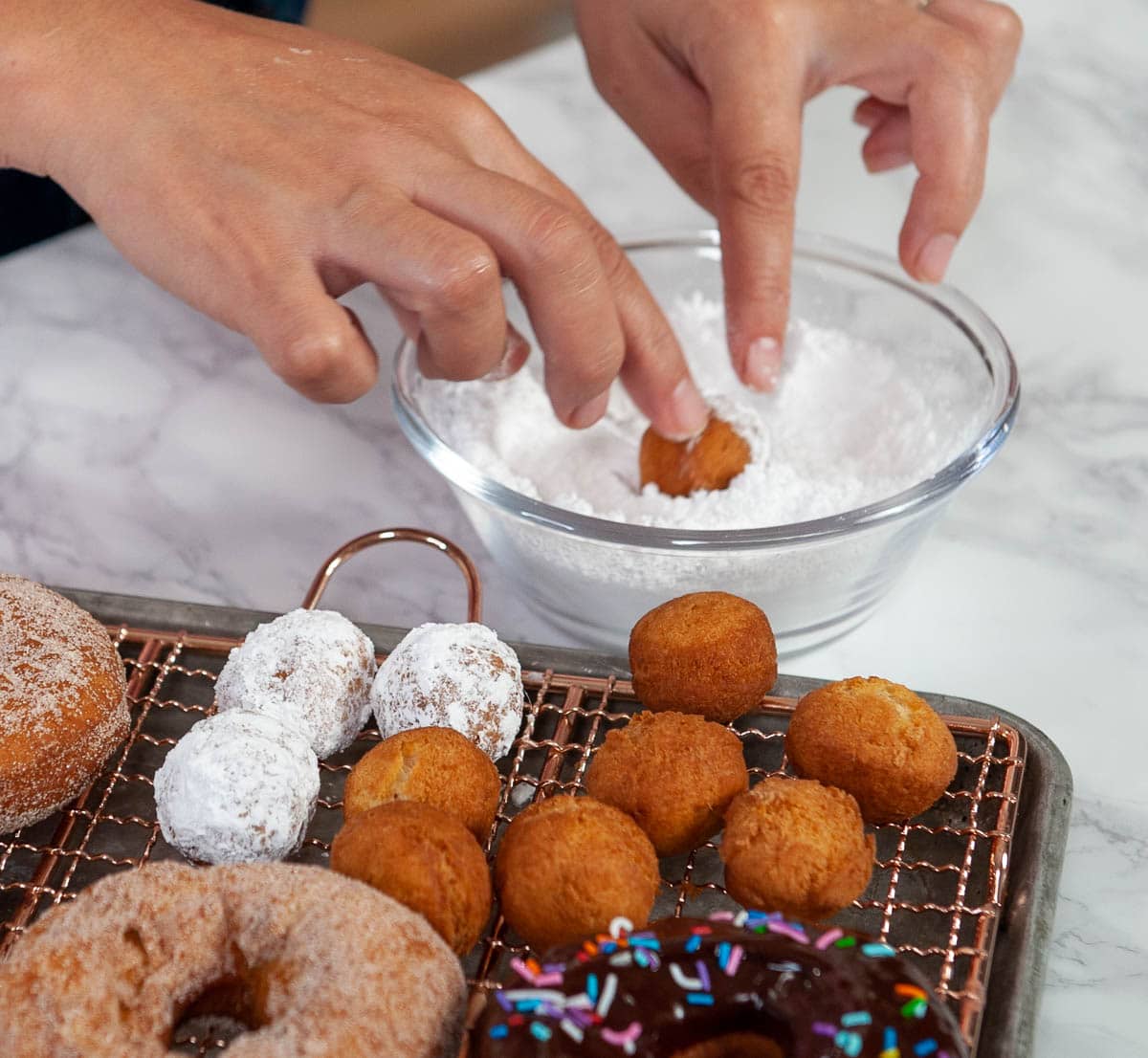 Dusting donut holes in powdered sugar.