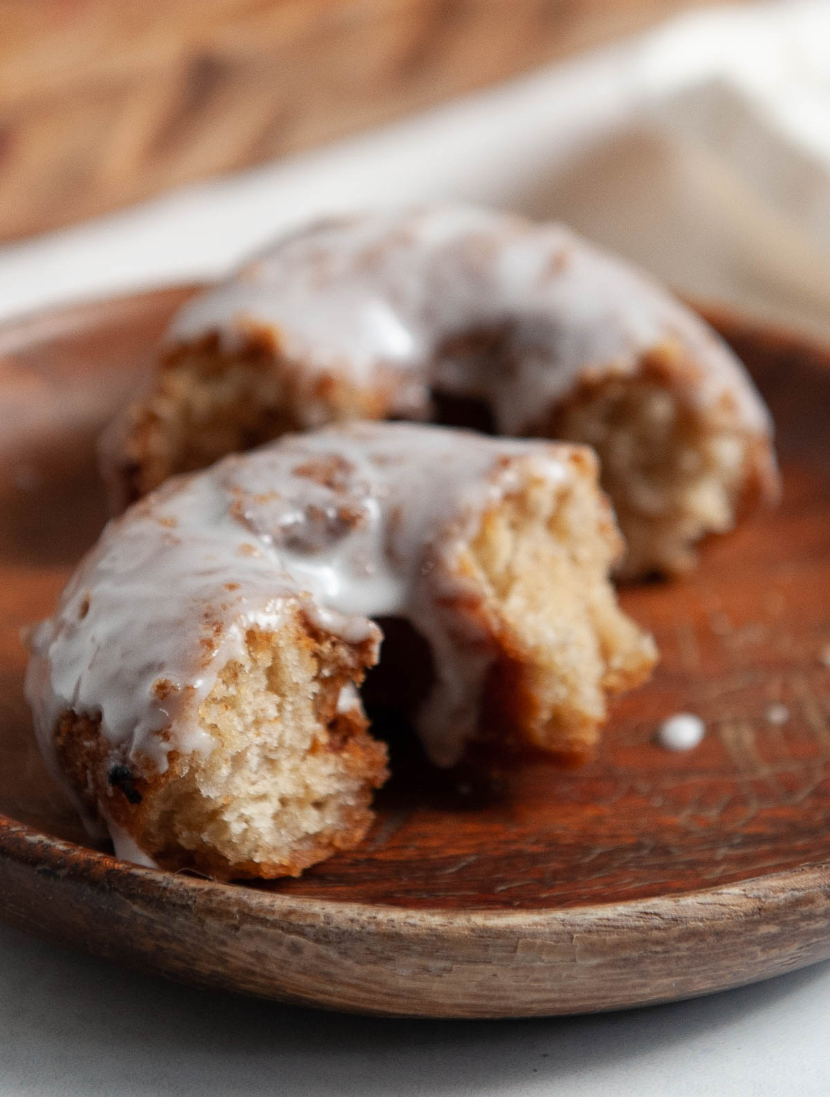 closeup of a glazed cake donut broken in half on a wooden plate