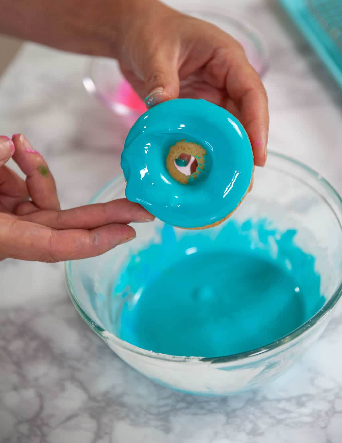 dunking a baked donut in blue donut glaze