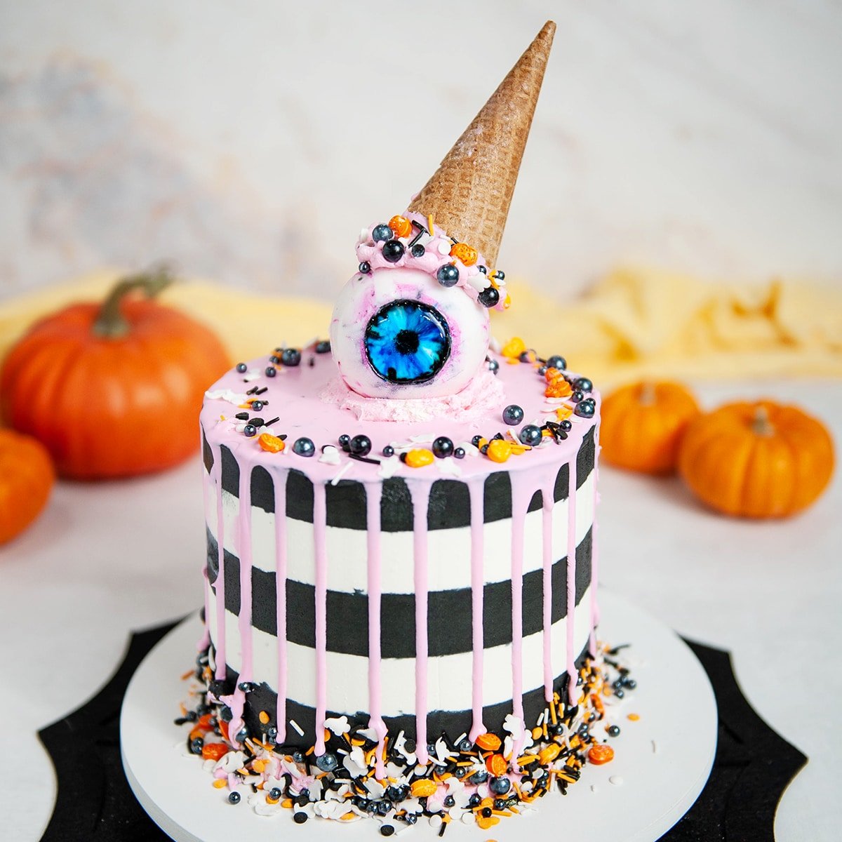 black and white striped cake with pink drip, gummy eyeball with ice cream cone on top