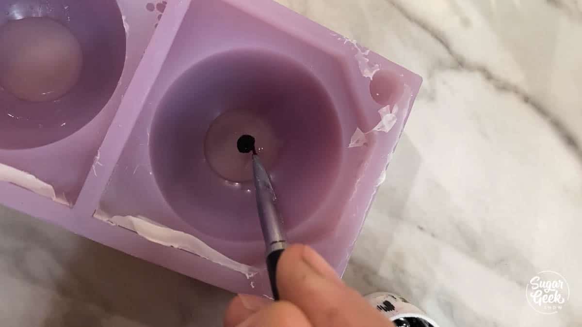 black paintbrush painting a black circle on clear gelatin inside a sphere mold