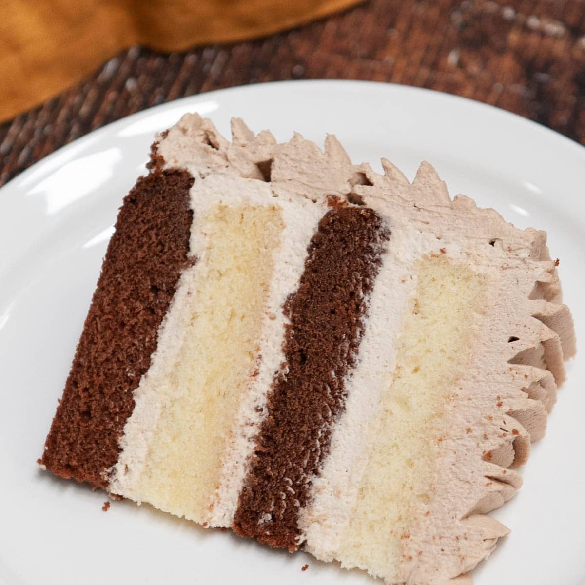 chocolate and vanilla cake slice with chocolate whipped cream on a white plate
