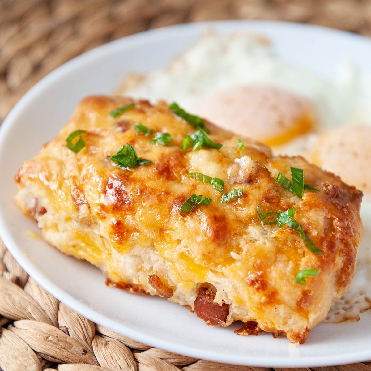 closeup of bacon cheddar scone on a white plate with eggs