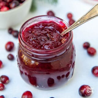 closeup of cranberry sauce in a clear jar with a spoon