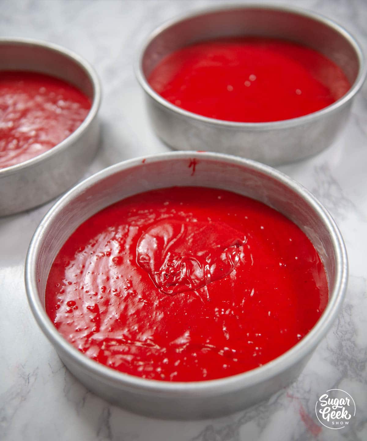 Red velvet cake batter in three cake pans