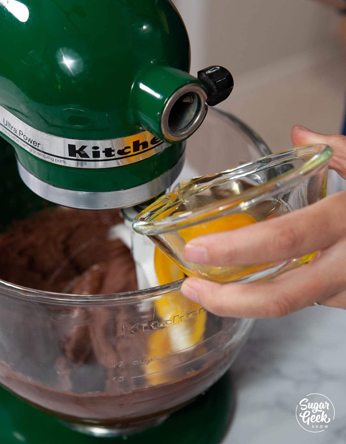 close up of hand holding clear glass bowl of eggs being added to cookie ingredients in a stand mixer