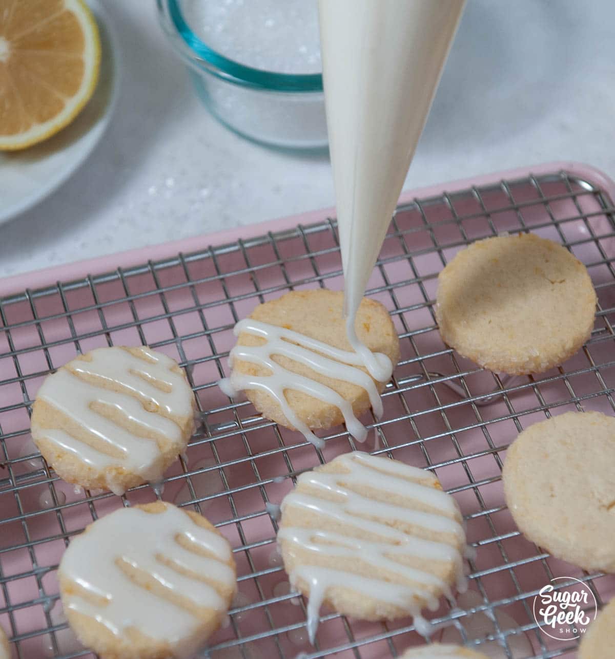 piping glaze onto baked lemon shortbread cookies on a cooling rack