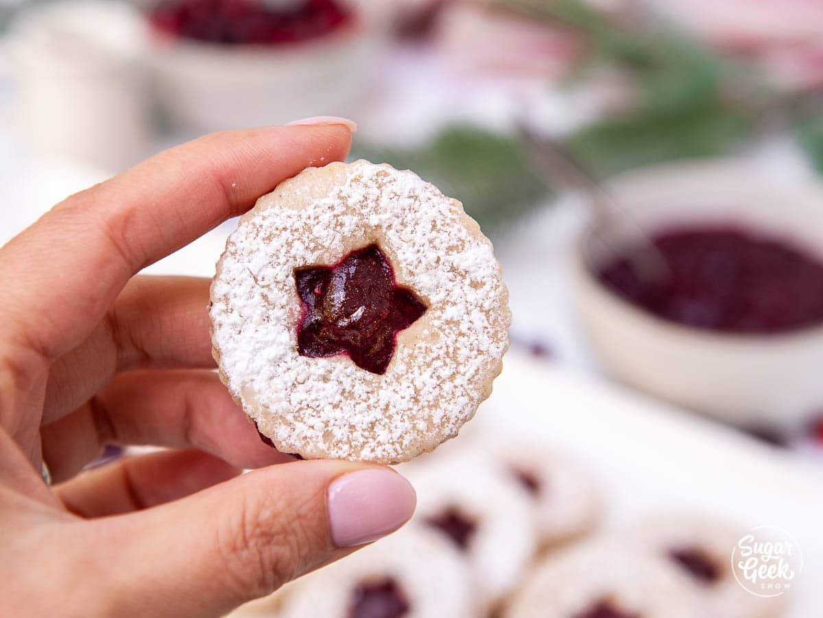 close up of a womans hand holding a linzer cookie