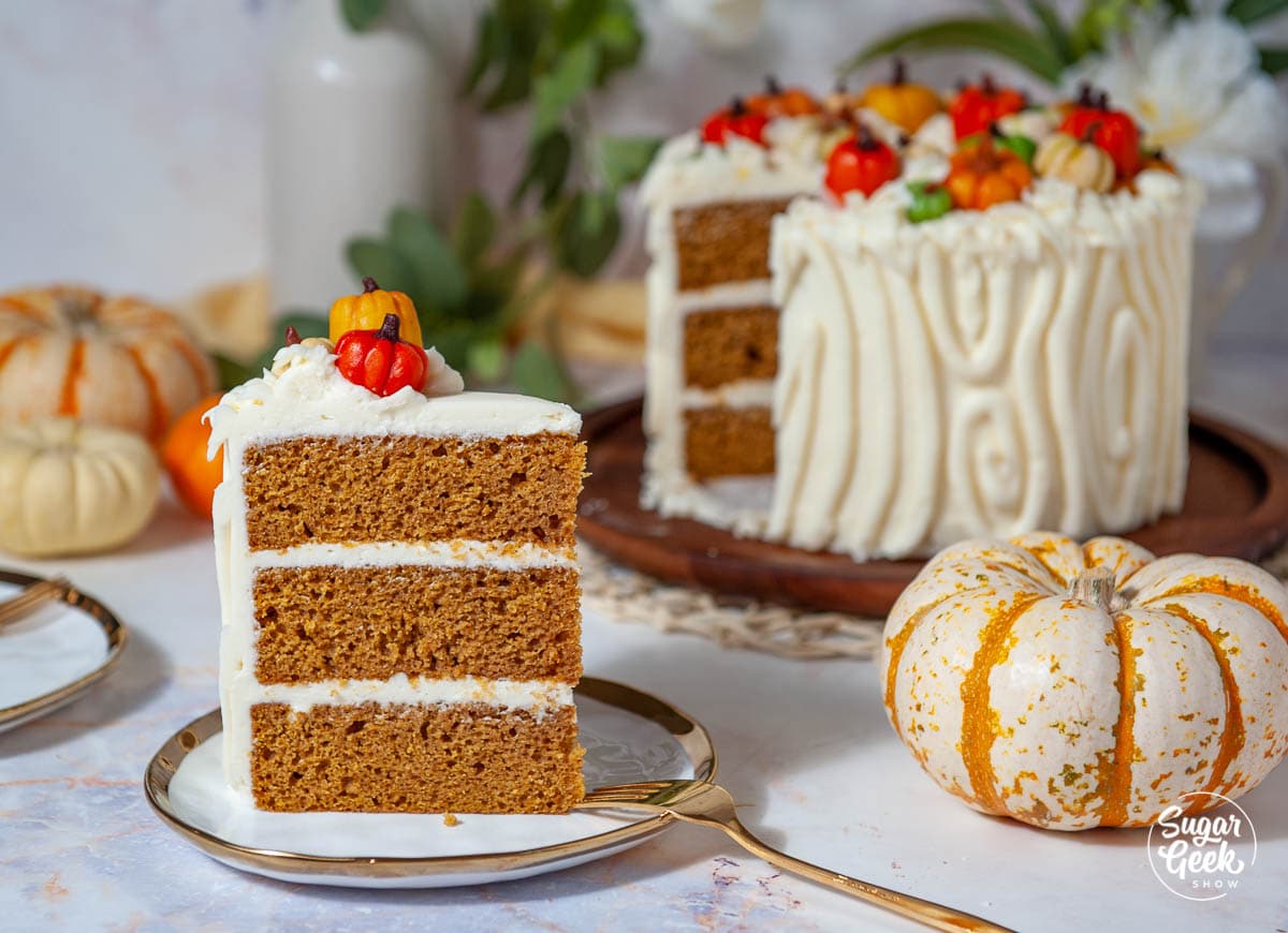 Slice of three-layer pumpkin spice cake on a plate in front of the decorated cake.
