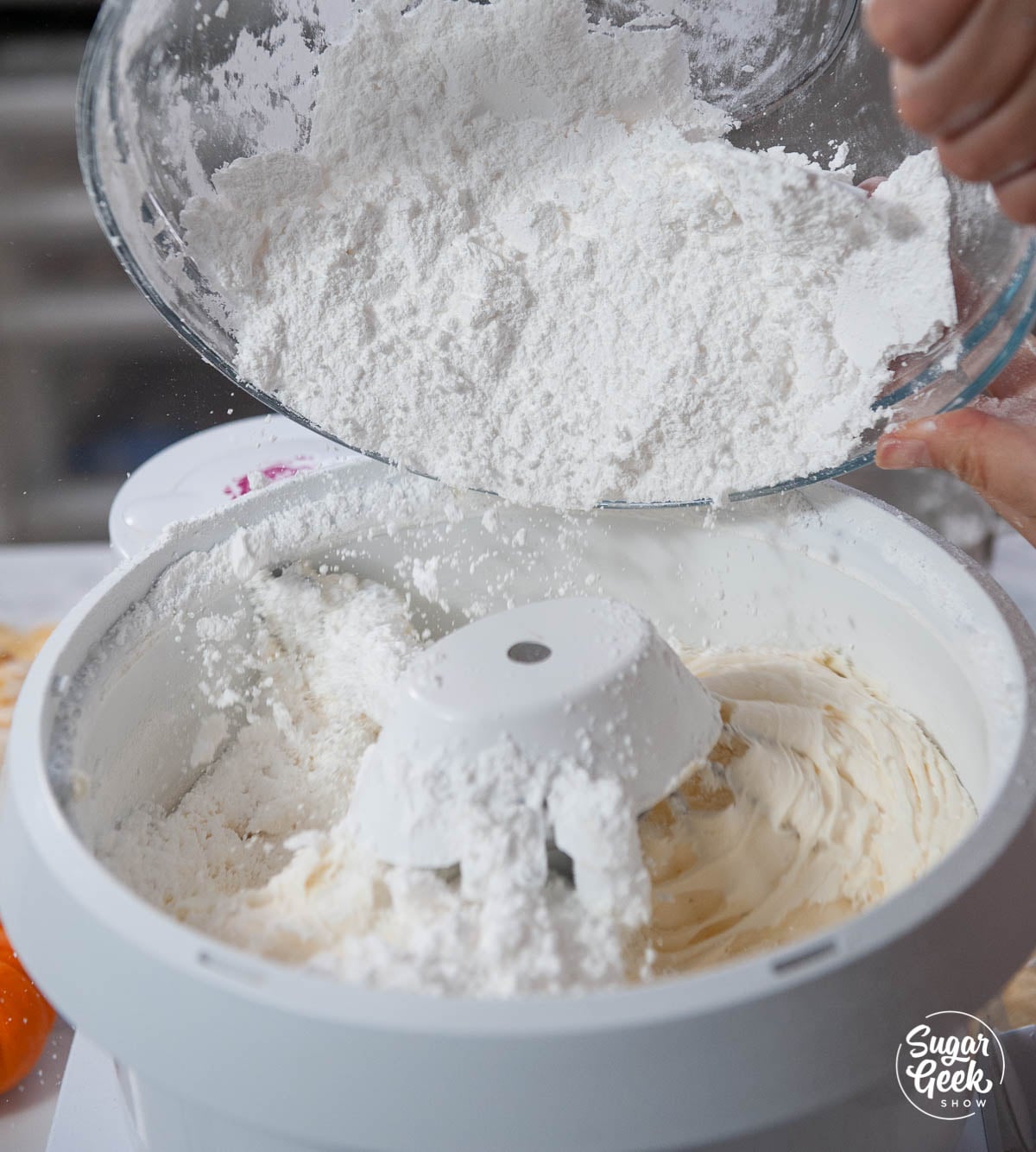 Cream cheese frosting mixture with a hand adding powdered sugar.