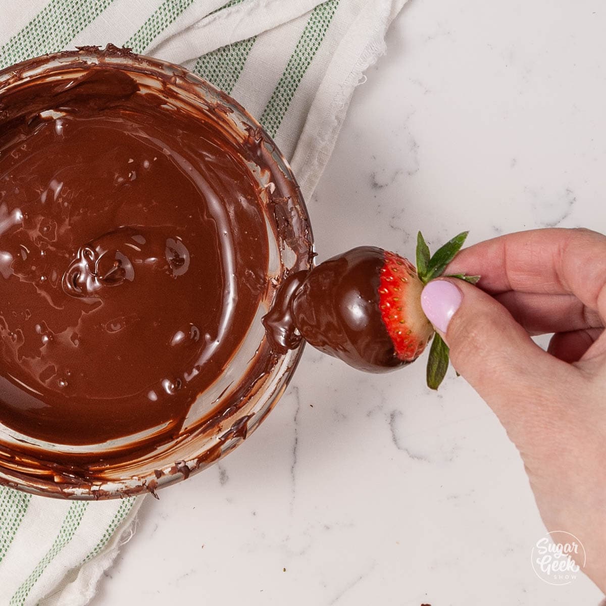 scraping a chocolate covered strawberry on the edge of a bowl from above