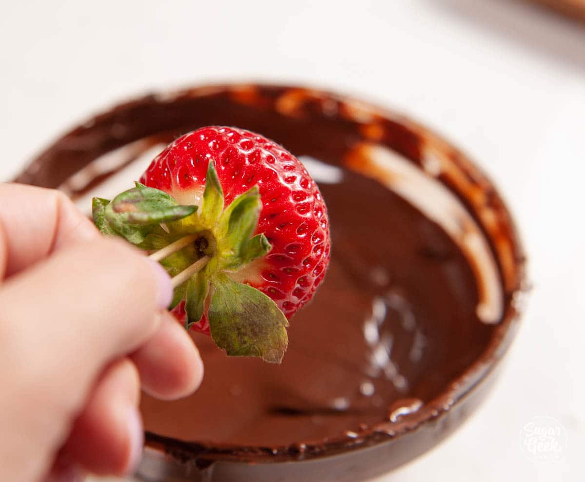 hand holding two toothpicks in a strawberry