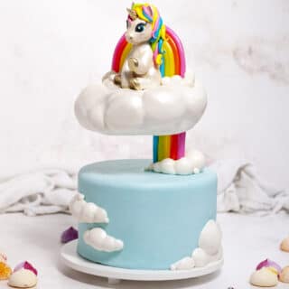 Cake with a floating cloud tier and rainbow with a unicorn cake topper sitting on top of it