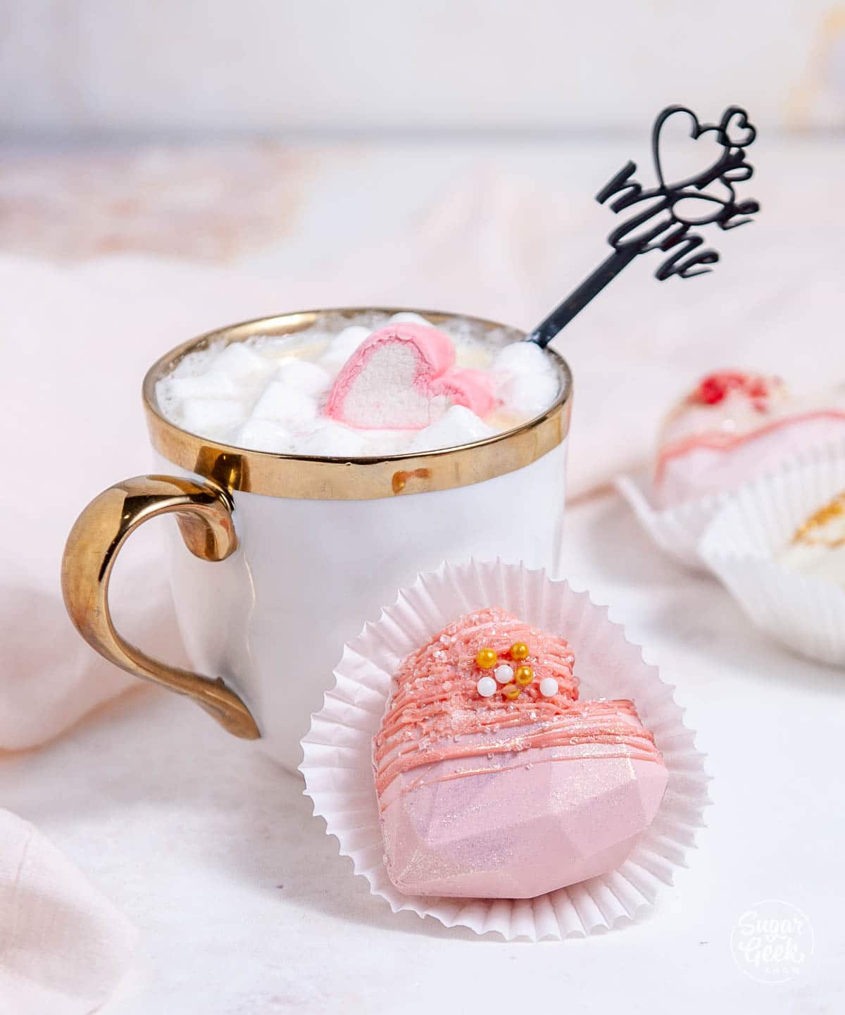heart hot chocolate bomb in front of a white mug with gold trim