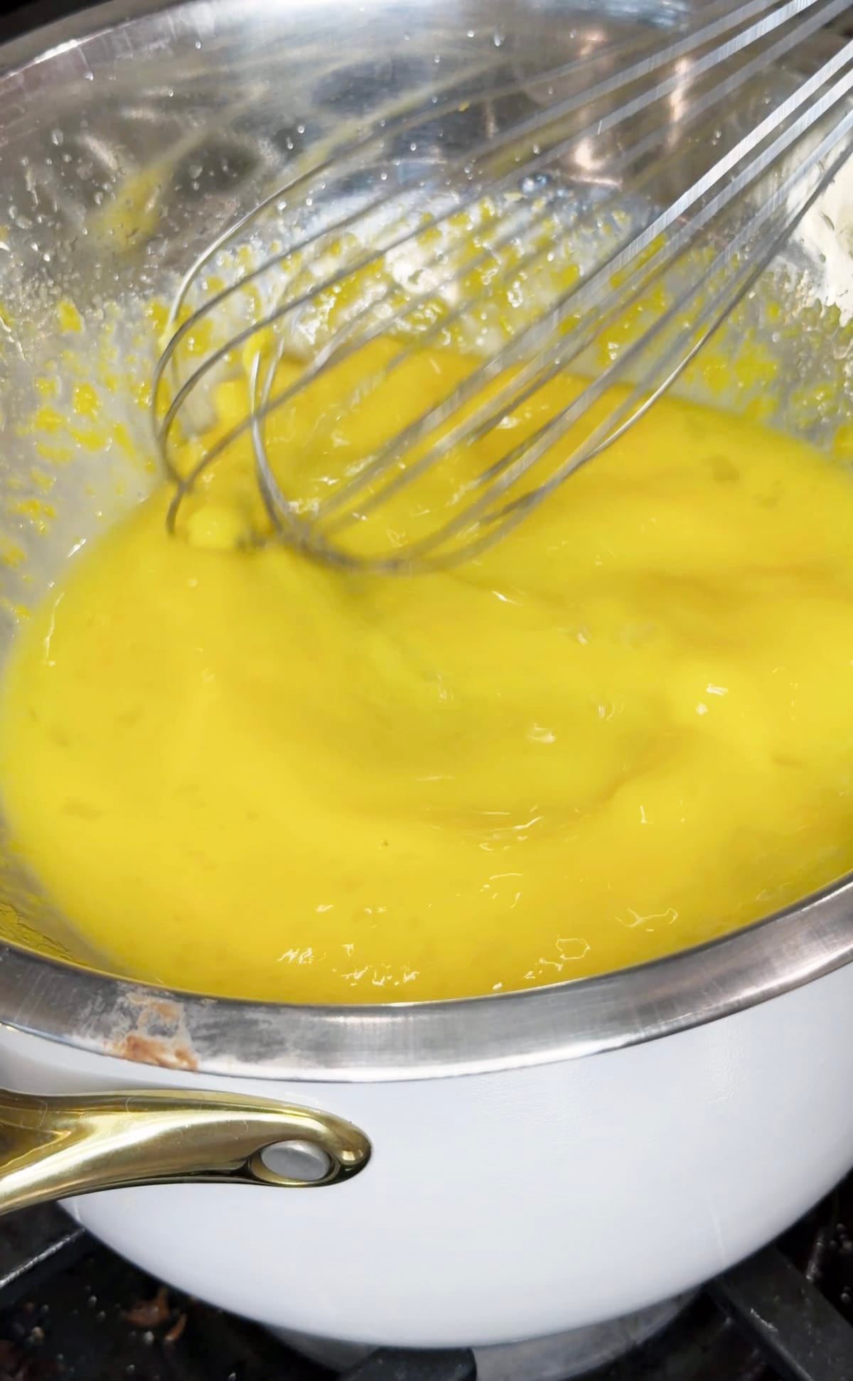 Thickened lemon curd over a white saucepan.