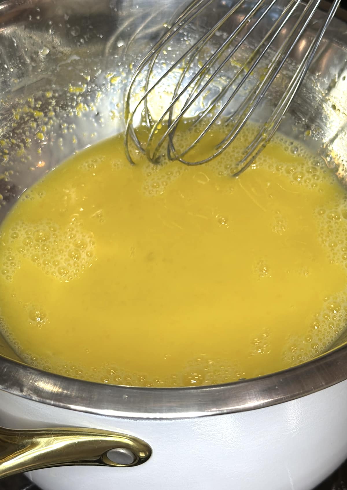 lemon curd ingredients in a metal bowl with a whisk over a white saucepan