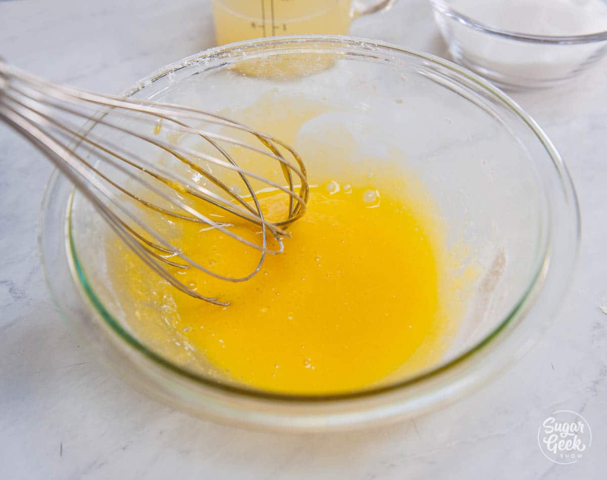 lemon curd ingredients in a clear bowl with a whisk
