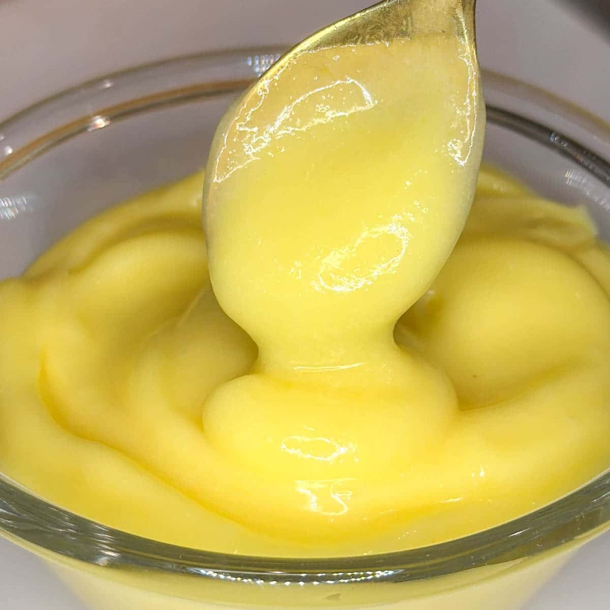 lemon curd on a gold spoon in a clear bowl