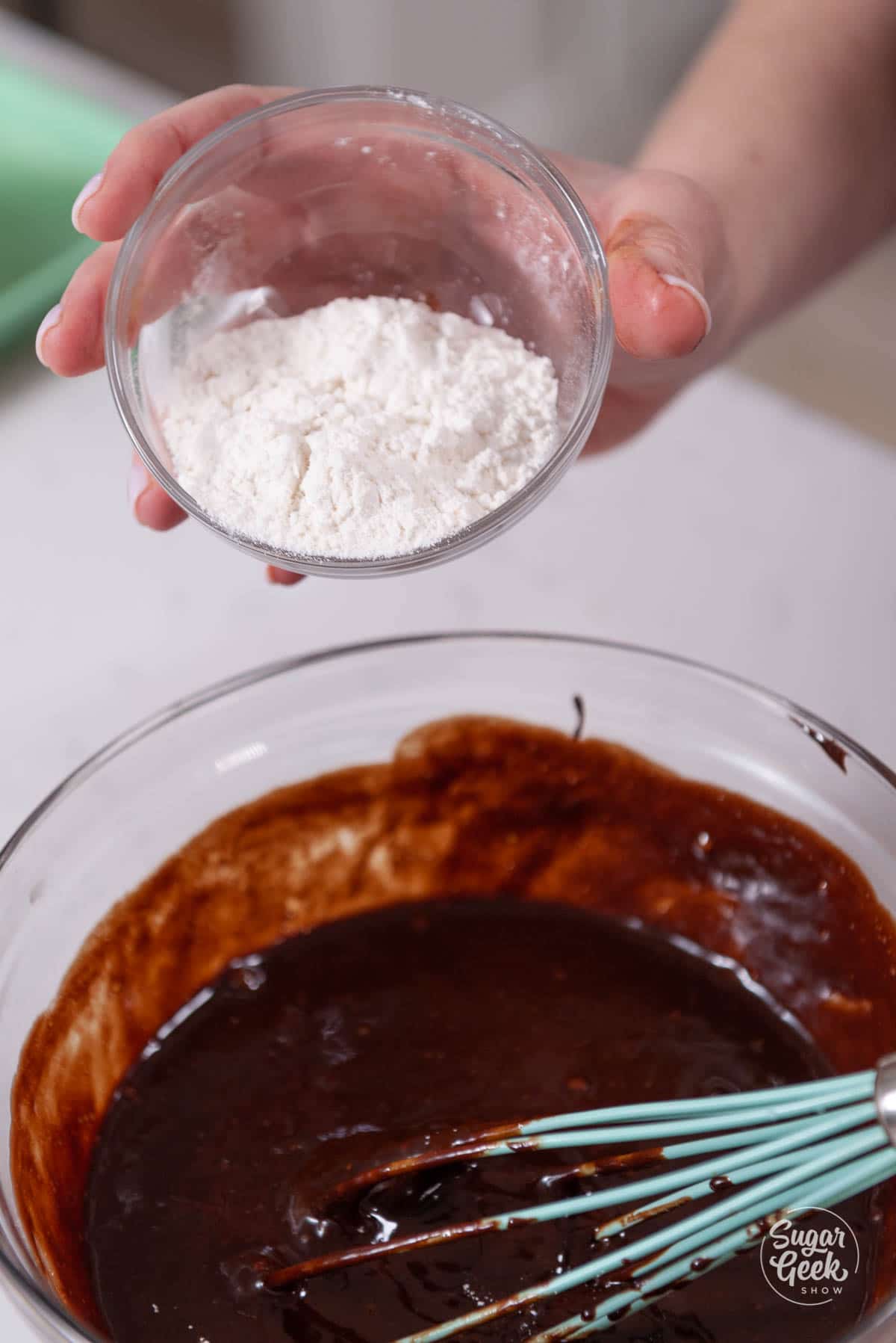 bowl of flour being held by a hand over a bowl of chocolate