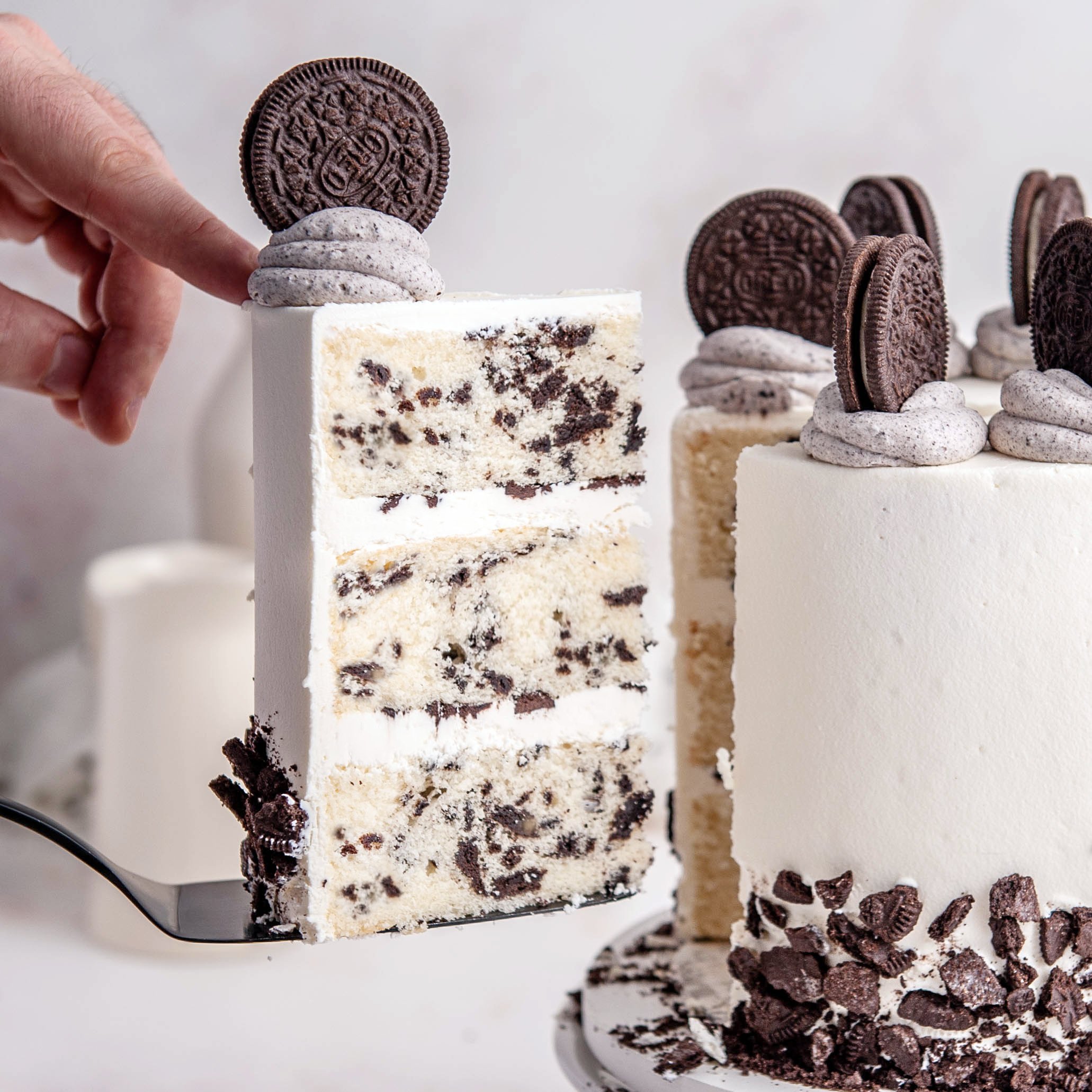 hand holding oreo cake slice next to oreo layer cake