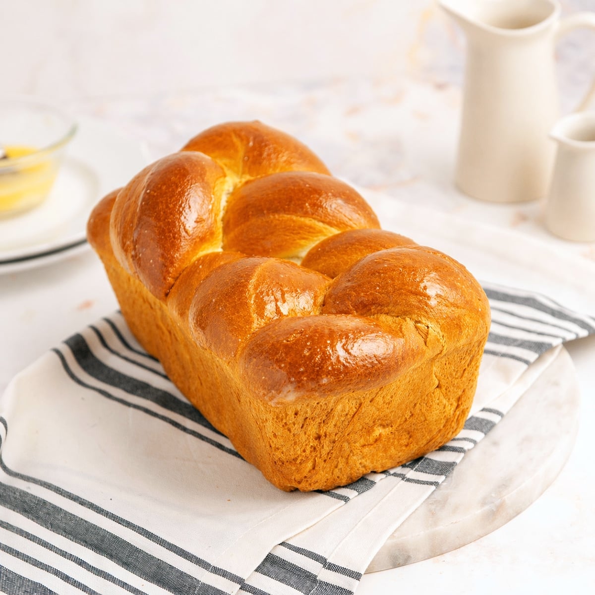 Braided loaf of brioche bread on a white towel with grey stripes.
