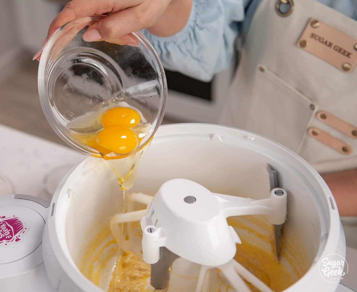 adding eggs to the yeast mixture in a mixing bowl