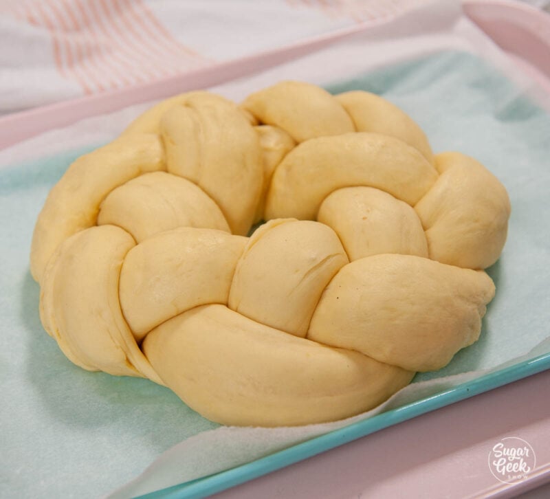 Braided brioche bread in a circle on a blue sheetpan.