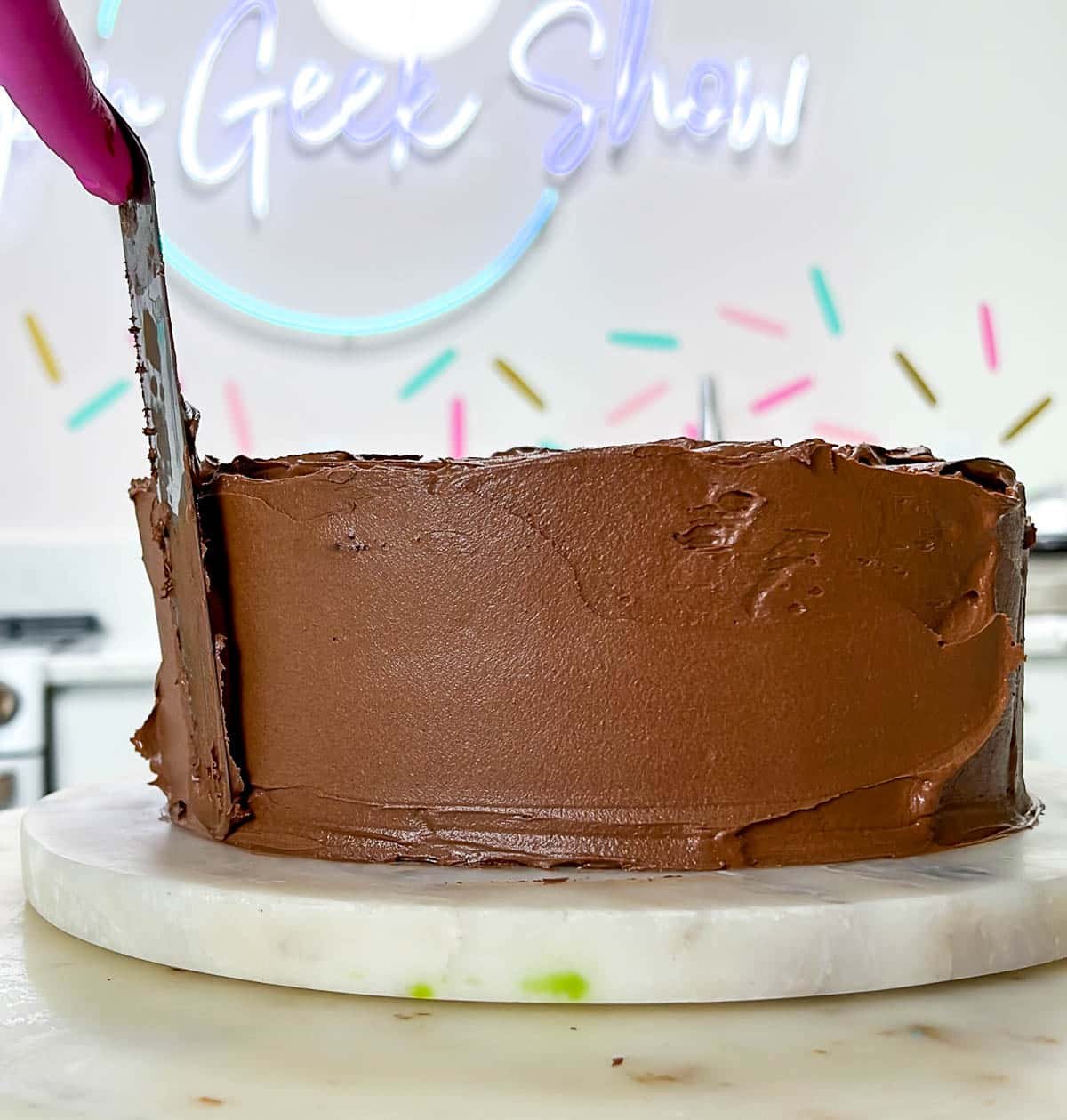 close up of frosting a chocolate cake with an offset spatula