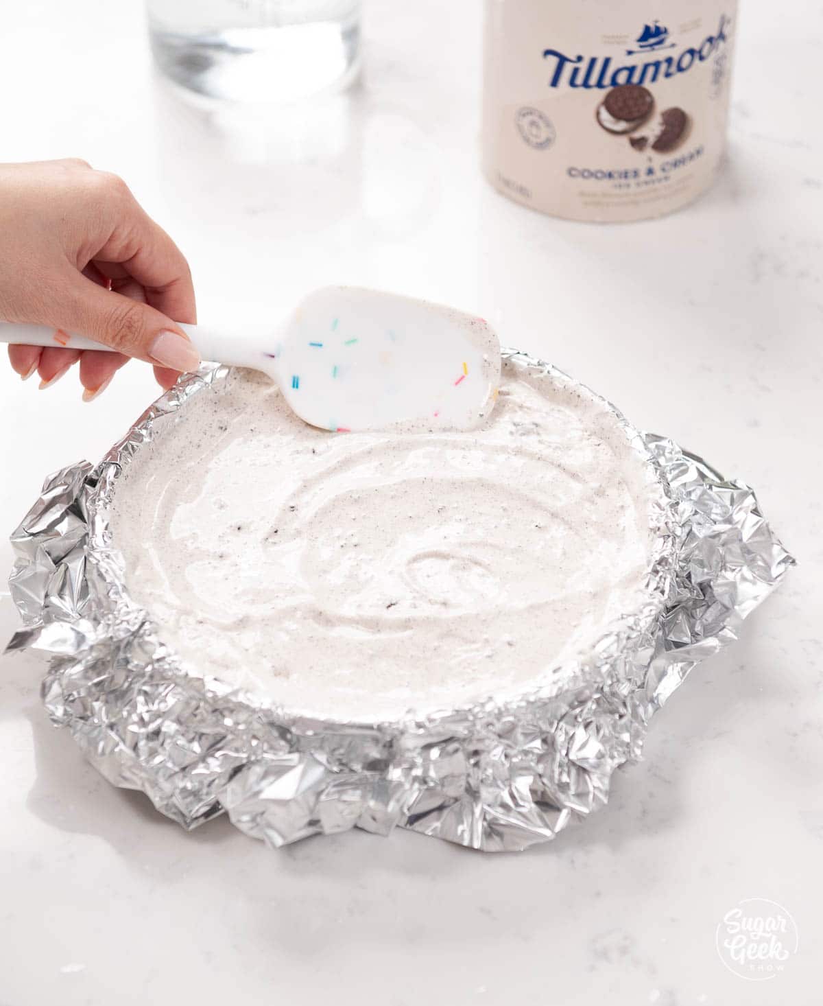 smoothing ice cream in aluminum foil pan with a spatula