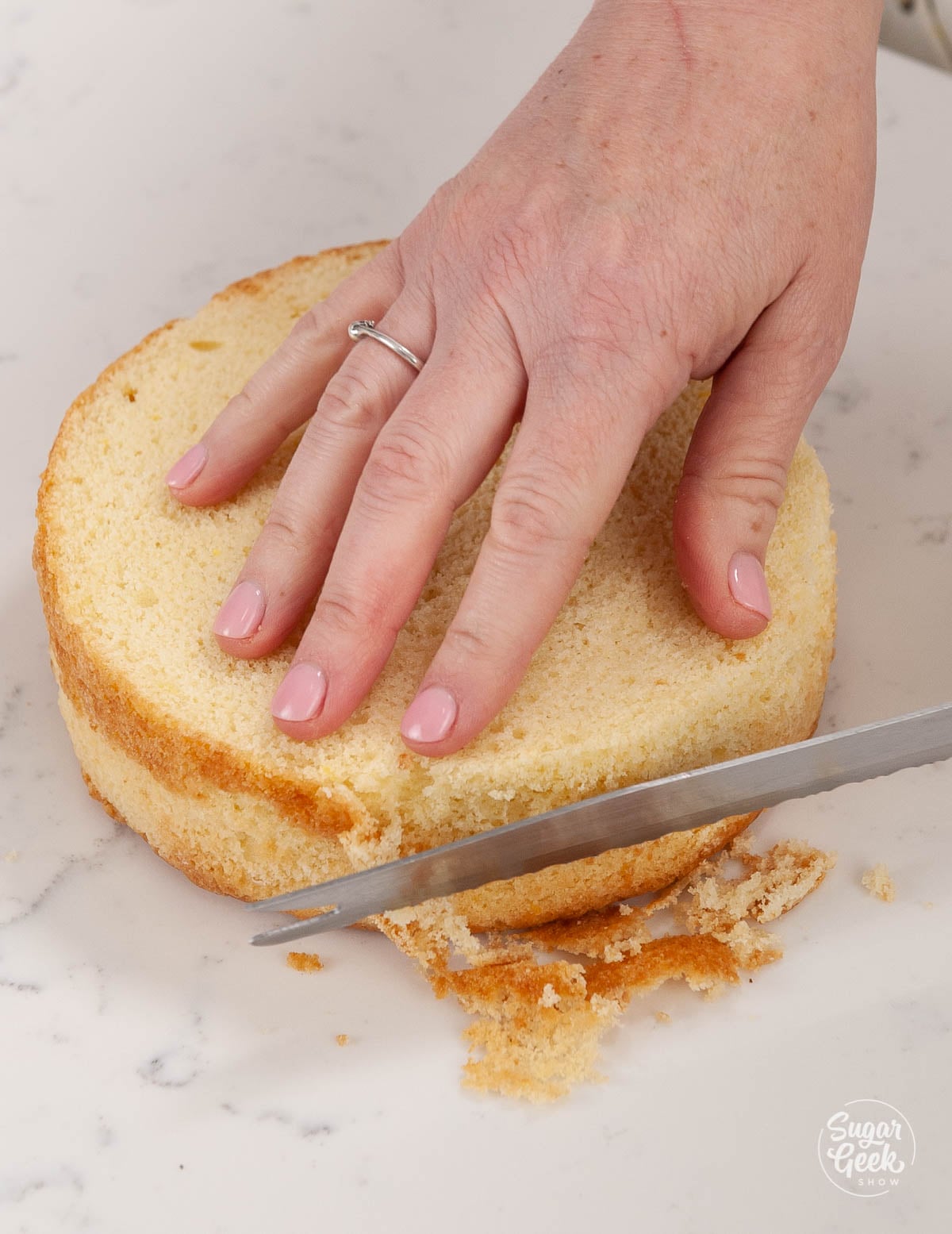Cutting brown sides of a cake layer with a serrated knife.