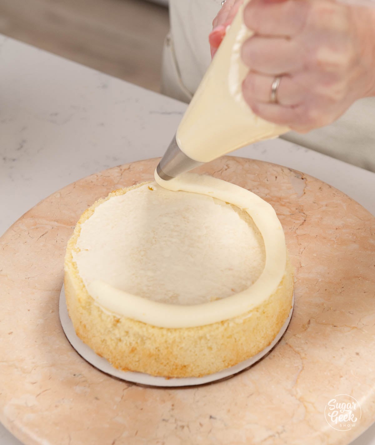 Piping a buttercream dam on top of a cake layer.