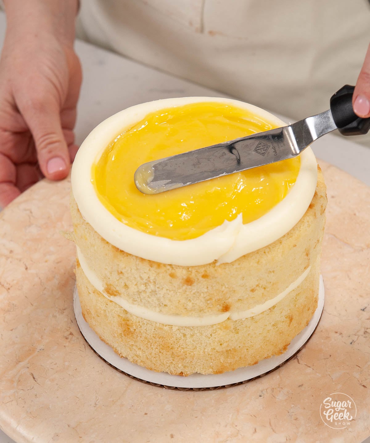 Smoothing lemon curd on top of a layer cake.