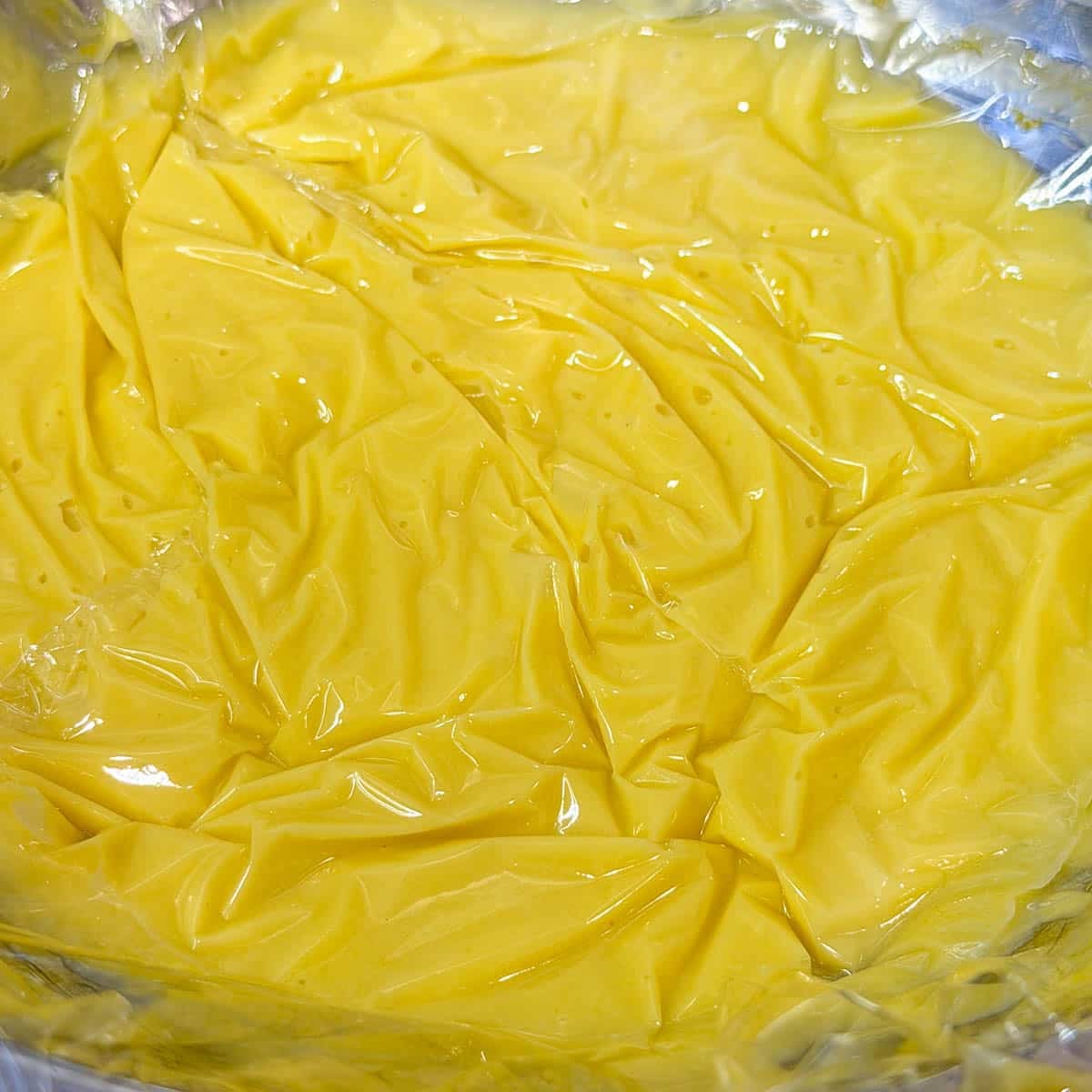 lemon curd in a metal bowl with plastic wrap on top