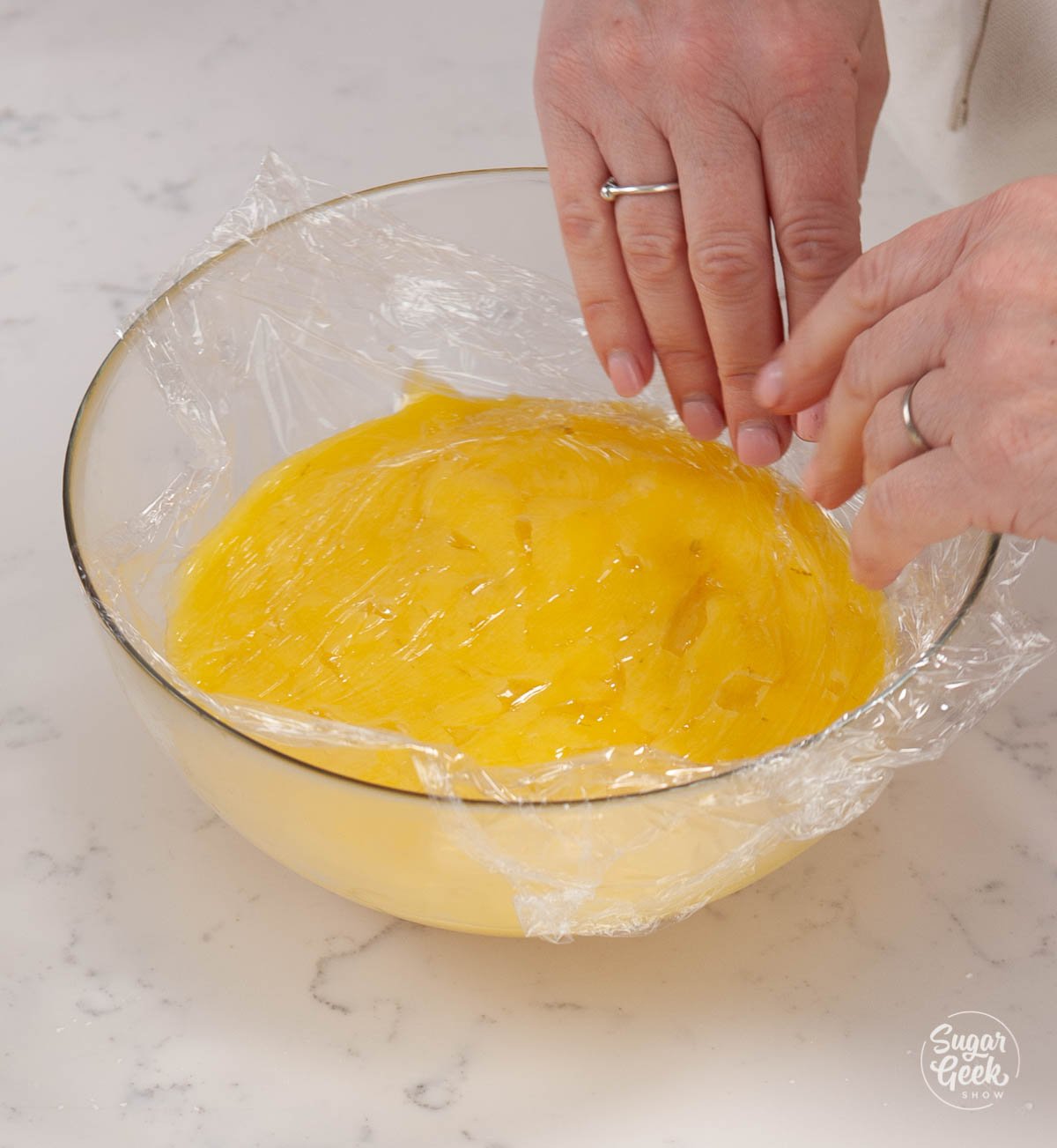 adding plastic wrap on top of lime curd in a clear bowl