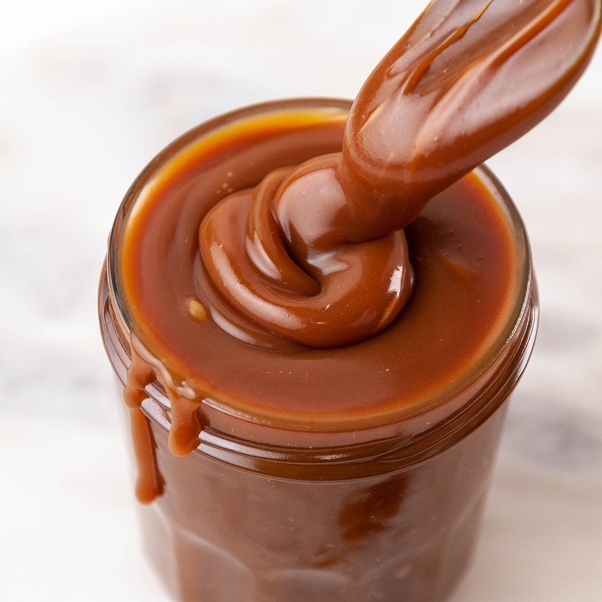 jar filled with creamy caramel sauce and a spoon covered in caramel