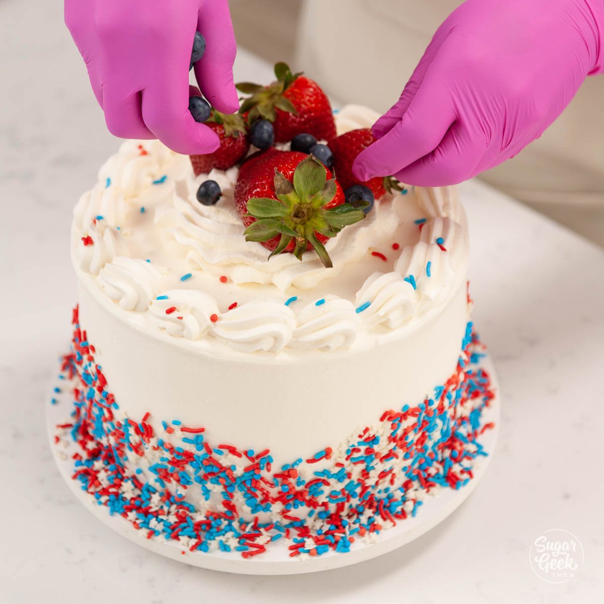 adding strawberries and blueberries to the top of the ice cream cake