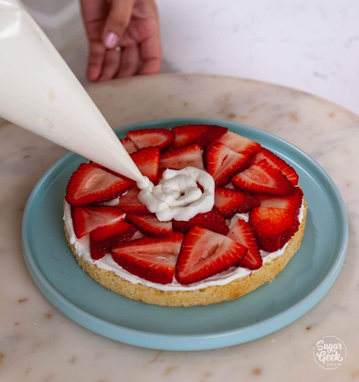 adding whipped cream to strawberries on a slice of cake