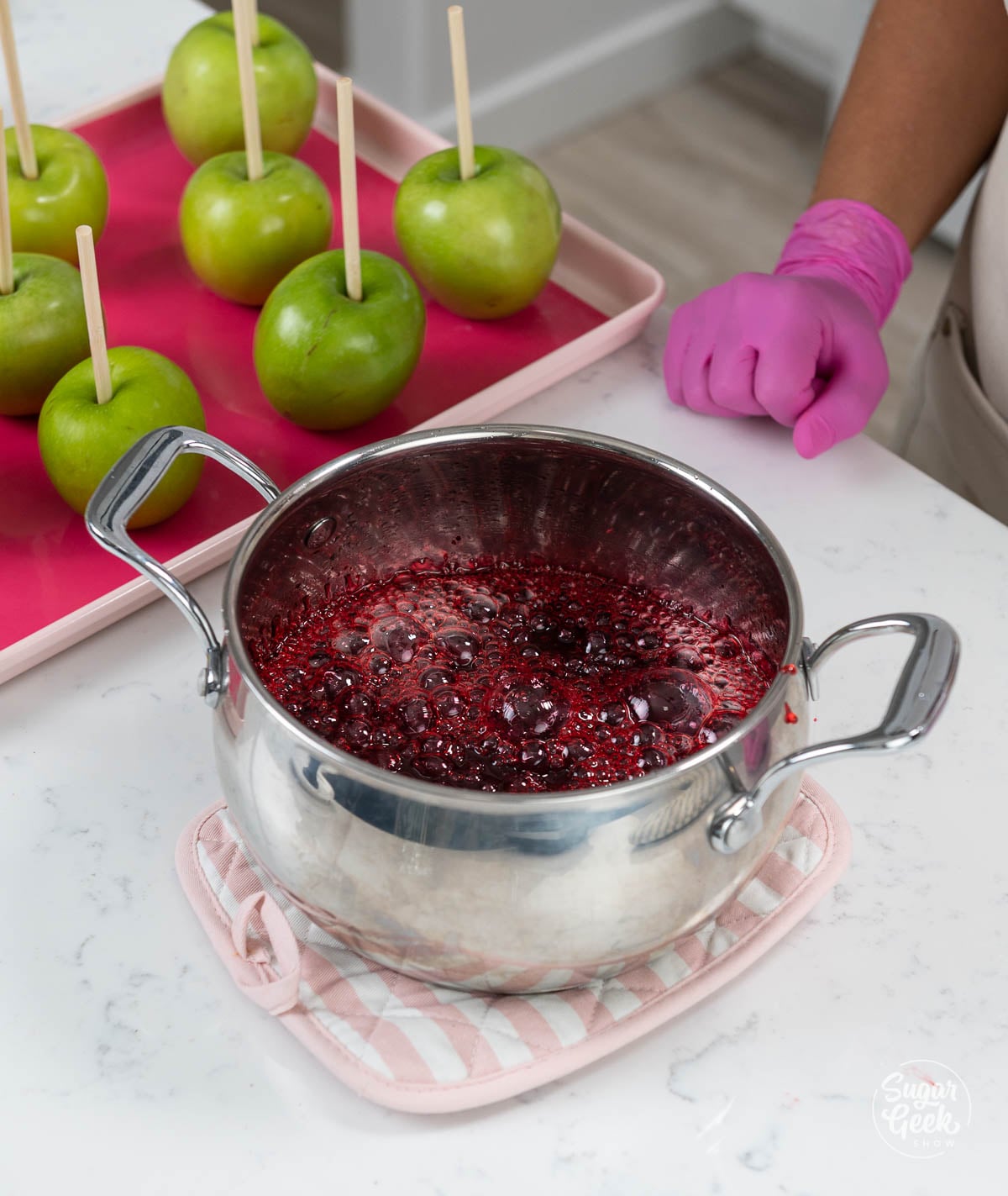 Red candy apple mixture bubbling in a pot off of the stovetop so it can cool down.