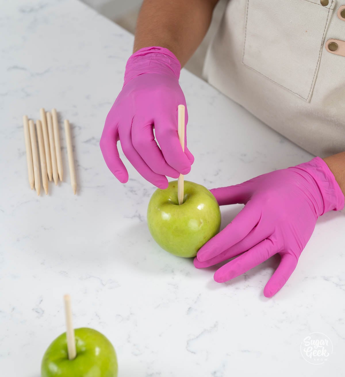 hands with pink gloves inserting apple sticks into green apples