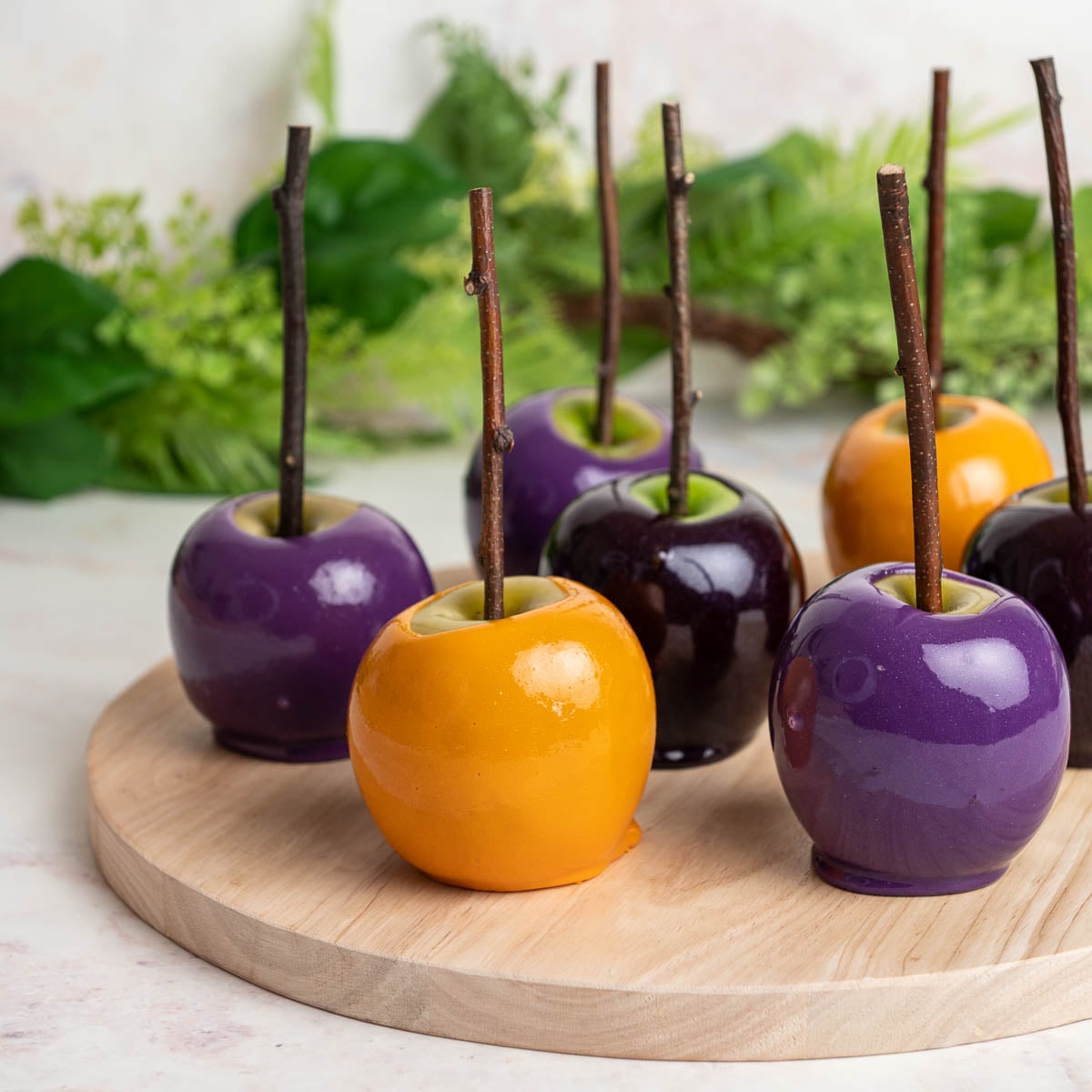 Yellow and purple candy apples on a wooden serving platter.