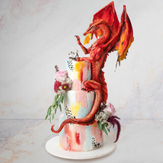 Wedding cake with a sculpted dragon sitting on top fighting bride and groom cake toppers