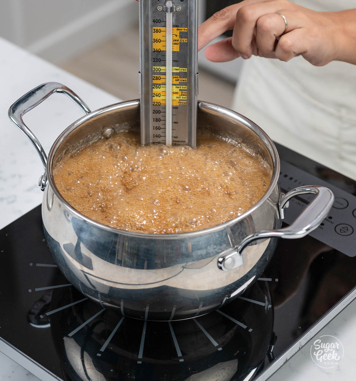 womans hand placing a candy thermometer into a saucepan of caramel cooking