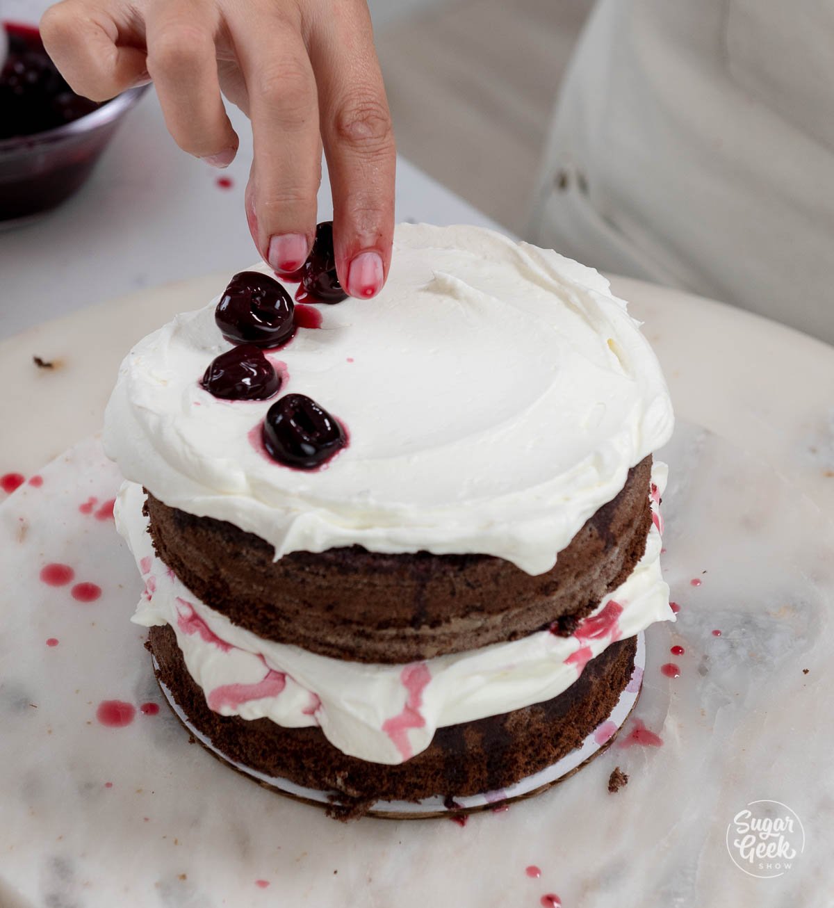 adding cherries to whipped cream on a cake